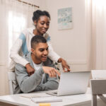 happy african american couple using laptop and pointing on screen at home