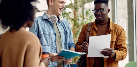 Group of happy college students talking while reading in a hallway.