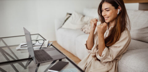 Cheerful millennial mixed race lady in glasses and wireless headphones has video call on laptop