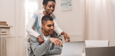 happy african american couple using laptop and pointing on screen at home