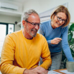 Senior middle aged happy couple using laptop together at home.