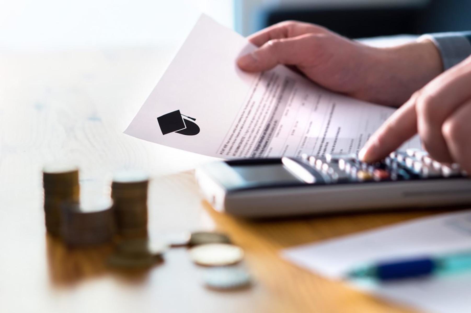 person reading student loan paperwork while using a calculator