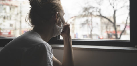 woman wearing mask looking out a window