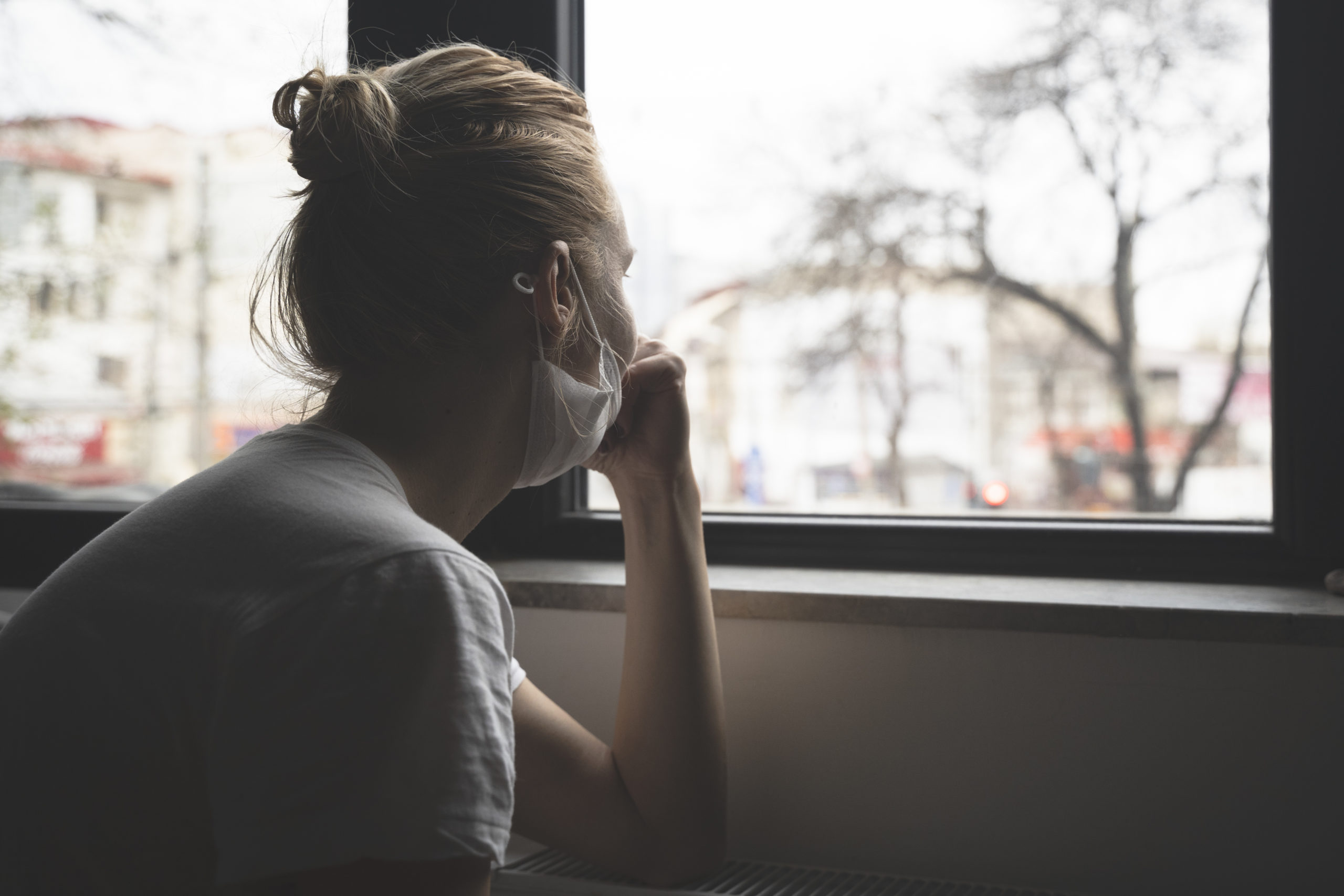 woman wearing mask looking out a window