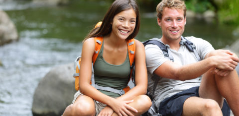 A hiking couple rest by a river while out on a date.