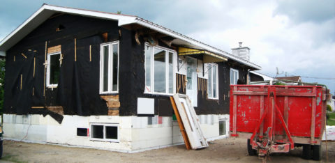 A fixer-upper being worked on, with its siding removed and a dumpster out front.