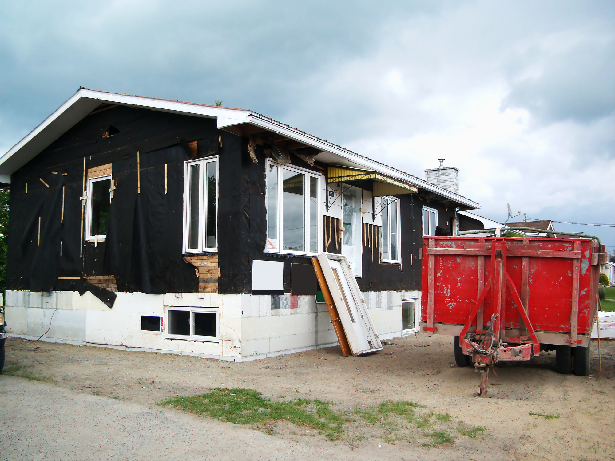 A fixer-upper being worked on, with its siding removed and a dumpster out front.