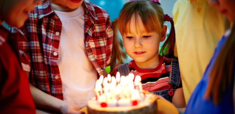 A small circle of children holding up a birthday cake for one to blow out the candles.