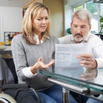 A frustrated couple — one seated in a wheelchair — looking over a medical bill.