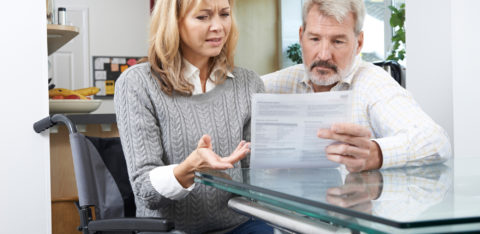 A frustrated couple — one seated in a wheelchair — looking over a medical bill.