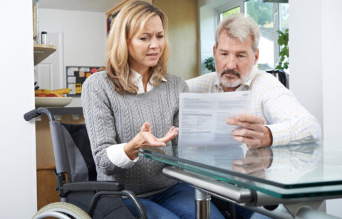 A frustrated couple — one seated in a wheelchair — looking over a medical bill.