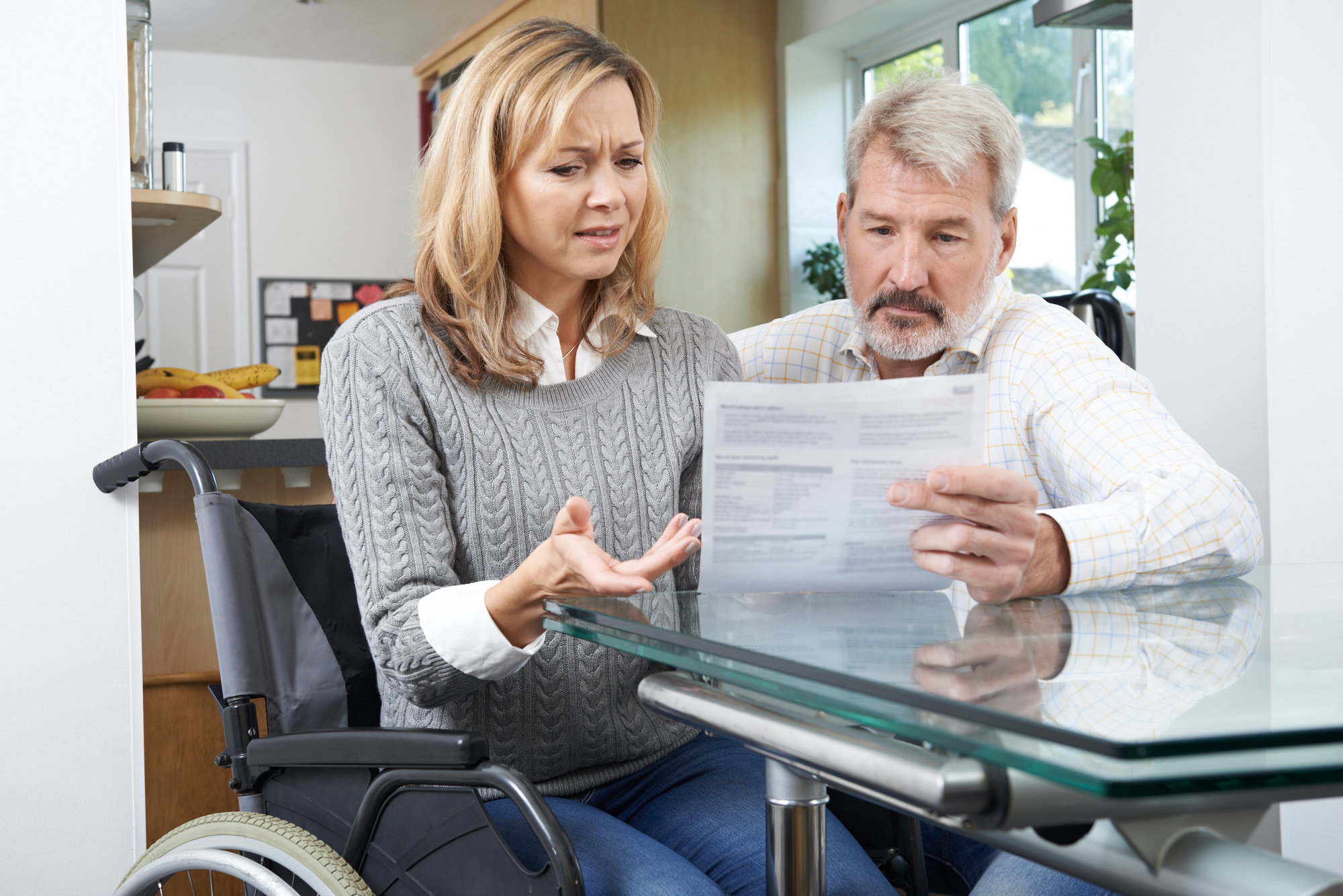 A frustrated couple — one seated in a wheelchair — looking over a medical bill.