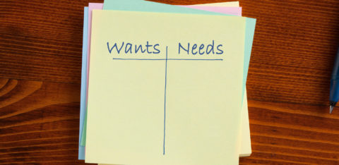 A piece of paper has a line drawn down the middle, splitting the words “wants” and “needs” written at the top.