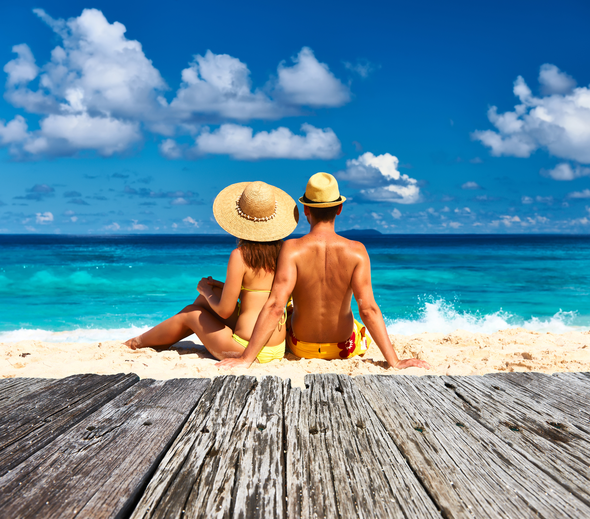 A couple on their honeymoon sitting on a tropical beach in their swimsuits.