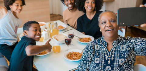 Five members of a multigenerational household pose at the dinner table to take a picture.