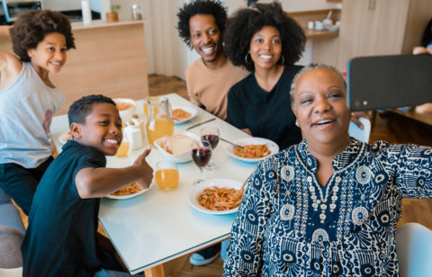 Five members of a multigenerational household pose at the dinner table to take a picture.