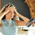 A worried person throws their hands on her head as a restaurant server extends a payment terminal toward them to pay the bill.