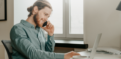 smiling young male talking on the phone and looking at computer