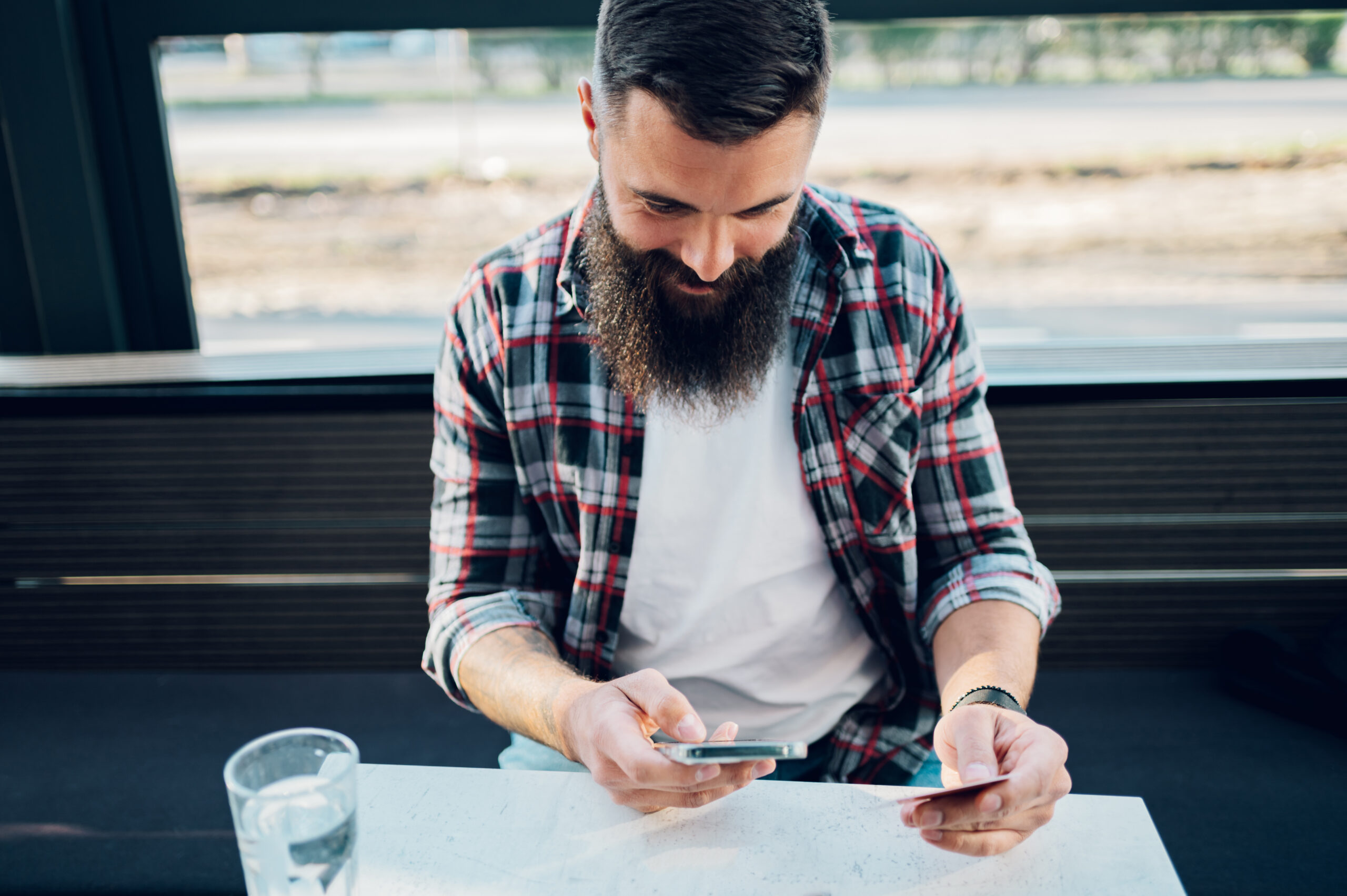 Bearded man using smartphone and a credit card in a cafe or restaurant