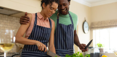 Happy young multiracial couple cooking meal together at kitchen island. people, togetherness and cooking concept, unaltered.