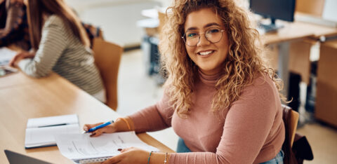 Happy female student having an exam at college classroom and looking at camera.