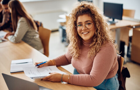 Happy female student having an exam at college classroom and looking at camera.