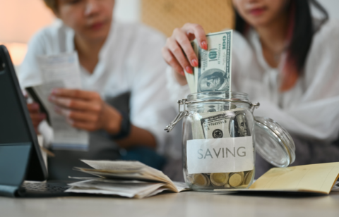 young couple putting money into a savings jar.