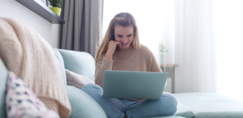 Happy woman at home using laptop sitting on sofa, online working