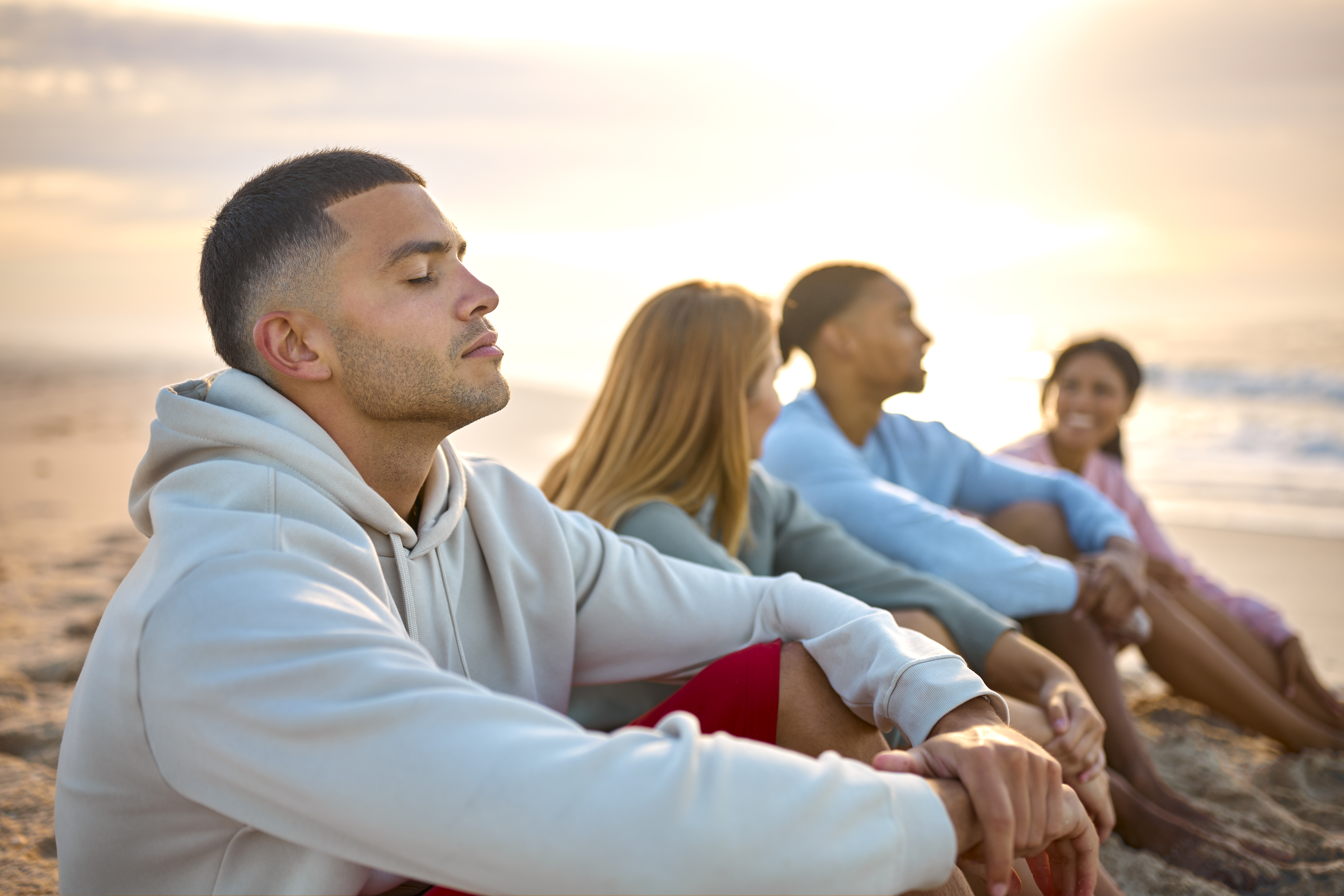 Man With Closed Eyes Relaxing With Friends On Vacation Sitting on beach thinking bout financial independence