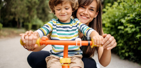 mom and toddler smiling and standing behind bike