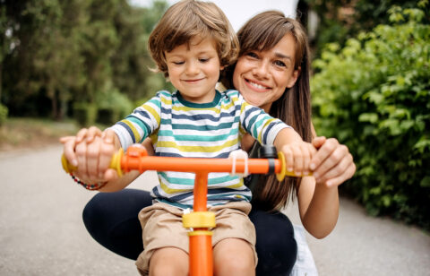 mom and toddler smiling and standing behind bike