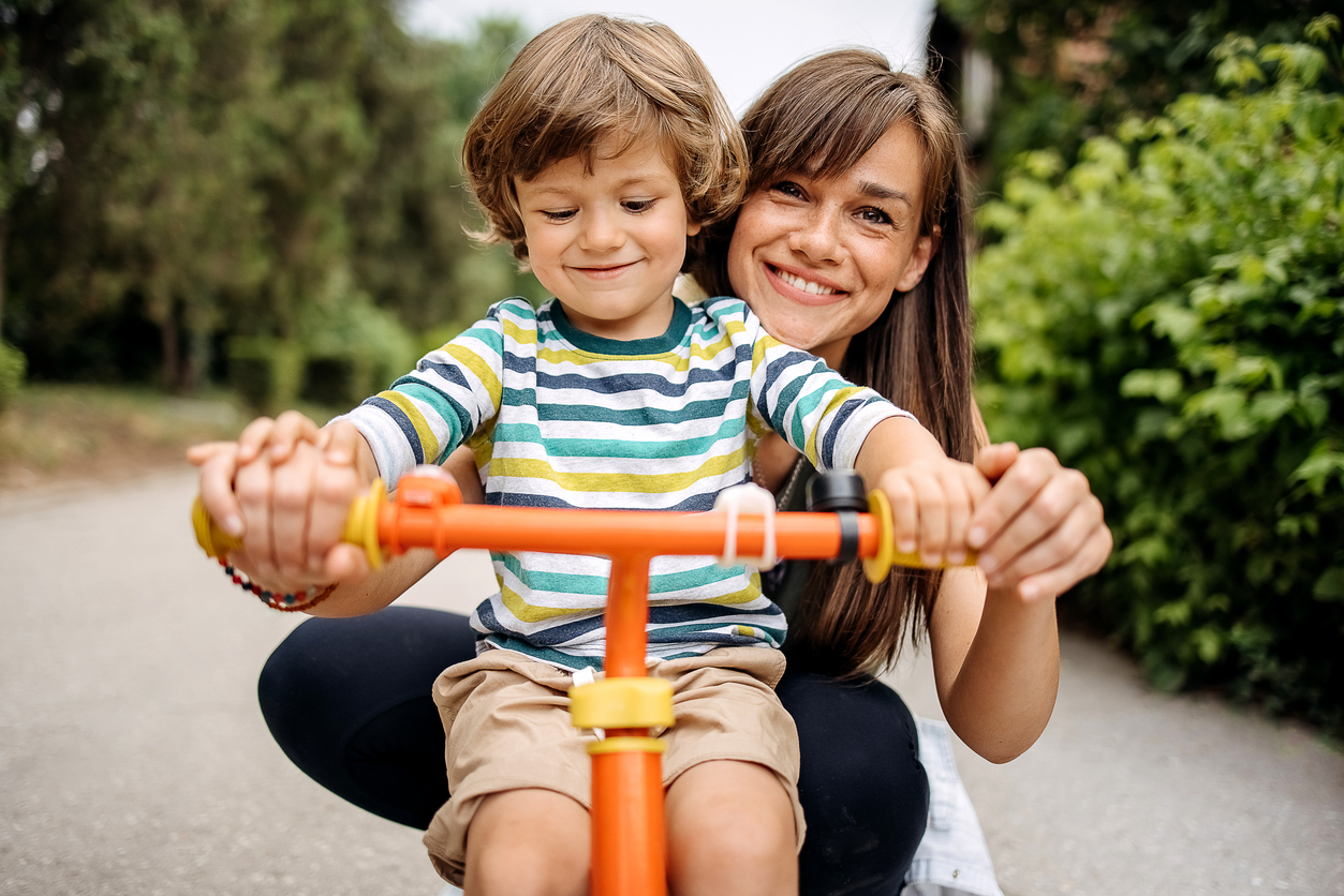 mom and toddler smiling and standing behind bike