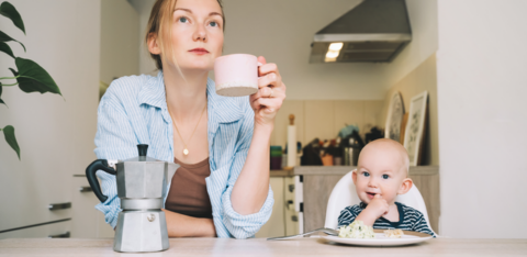 mom pondering and holding cup while baby eats next to her